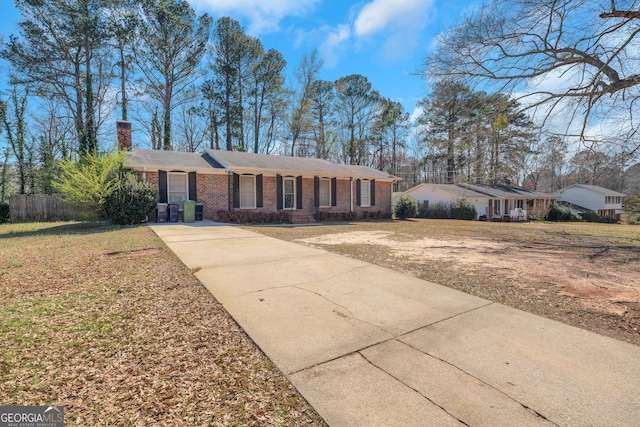 ranch-style home featuring driveway, fence, a front yard, brick siding, and a chimney