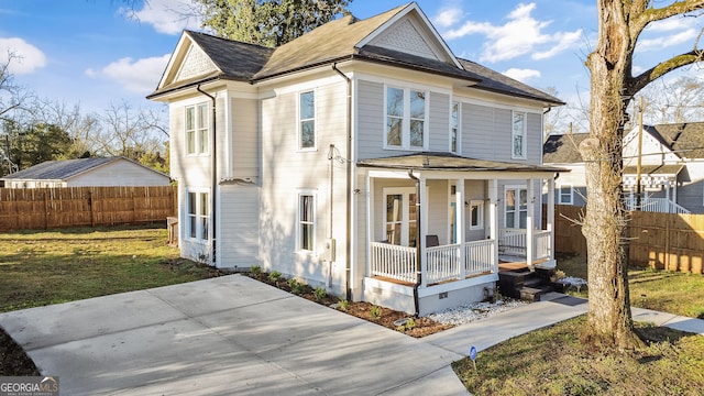 view of front facade featuring roof with shingles, covered porch, a front yard, and fence