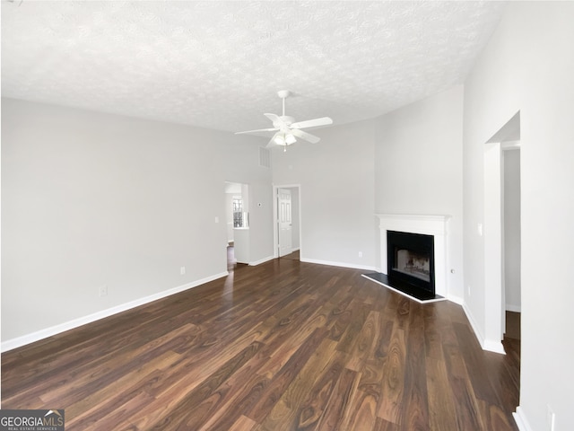 unfurnished living room with a fireplace with raised hearth, dark wood-type flooring, baseboards, vaulted ceiling, and a textured ceiling