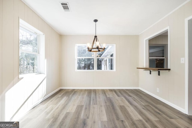 unfurnished dining area featuring visible vents, ornamental molding, wood finished floors, baseboards, and a chandelier