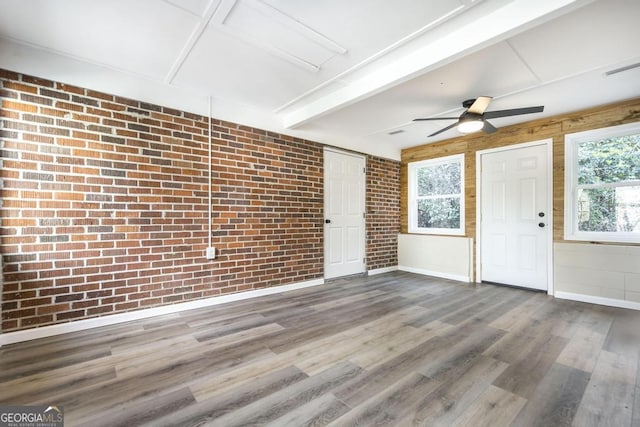 interior space featuring a ceiling fan, wood finished floors, baseboards, brick wall, and beamed ceiling