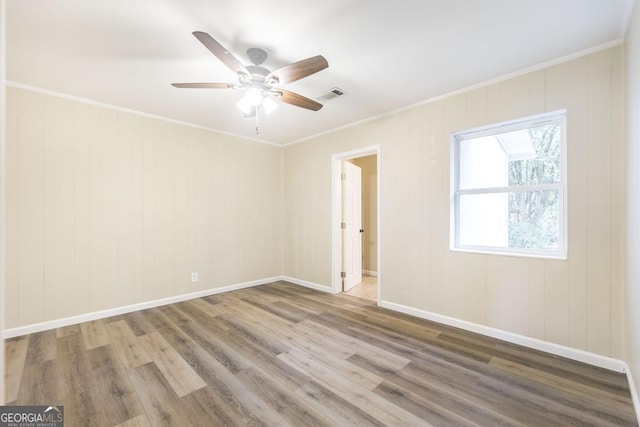 spare room featuring crown molding, wood finished floors, visible vents, and baseboards