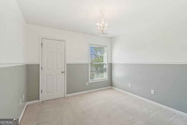 carpeted empty room featuring baseboards and a chandelier