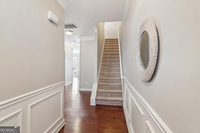 corridor with visible vents, dark wood-style flooring, ornamental molding, stairs, and a decorative wall