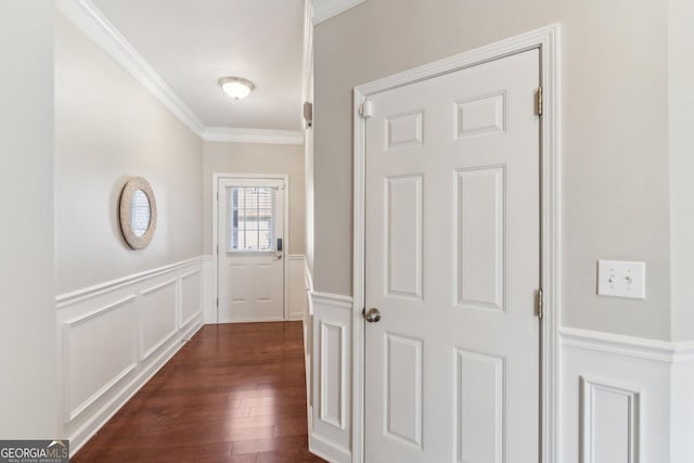 hallway featuring a wainscoted wall, dark wood finished floors, crown molding, and a decorative wall