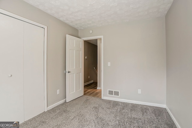 unfurnished bedroom featuring baseboards, visible vents, a textured ceiling, and carpet