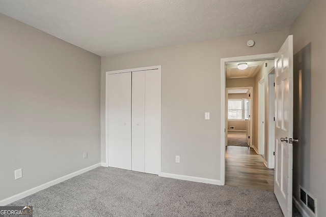 unfurnished bedroom with a textured ceiling, carpet, visible vents, and baseboards