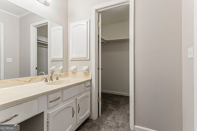 bathroom with a walk in closet, baseboards, vanity, and crown molding