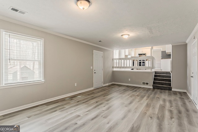 unfurnished living room with light wood-style flooring, visible vents, and ornamental molding