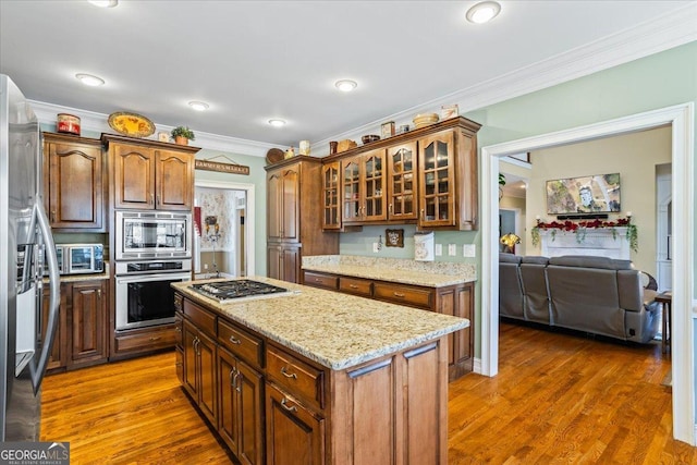 kitchen featuring ornamental molding, light stone counters, wood finished floors, stainless steel appliances, and glass insert cabinets