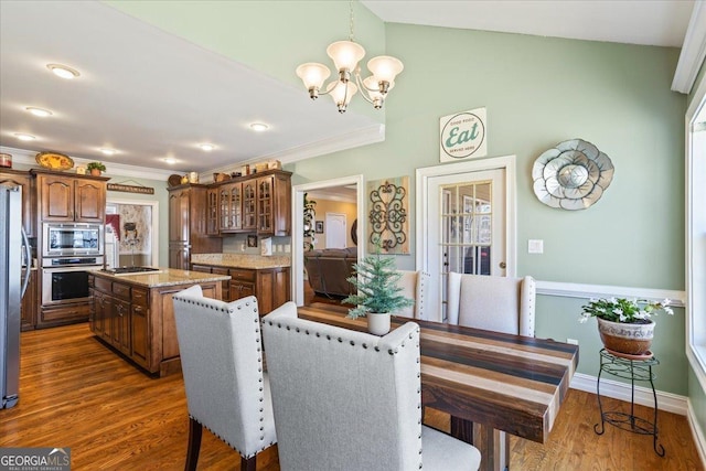 dining space with a notable chandelier, dark wood-style floors, vaulted ceiling, and ornamental molding