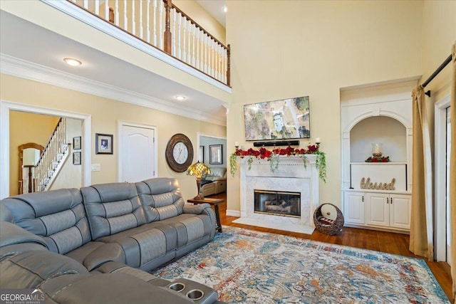 living area with a high end fireplace, stairway, a high ceiling, crown molding, and dark wood-style flooring