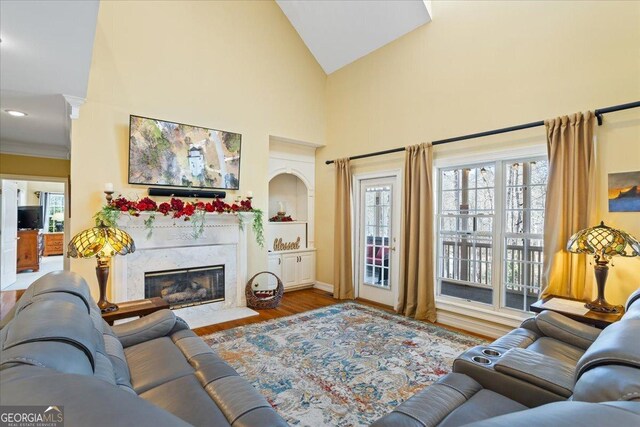 living area with a high end fireplace, ornamental molding, decorative columns, wood finished floors, and high vaulted ceiling