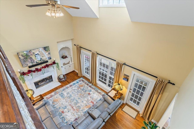 living room with a high end fireplace, high vaulted ceiling, a ceiling fan, and wood finished floors