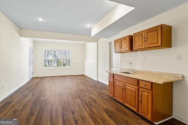 kitchen featuring brown cabinets, a sink, light stone counters, dark wood-style floors, and baseboards