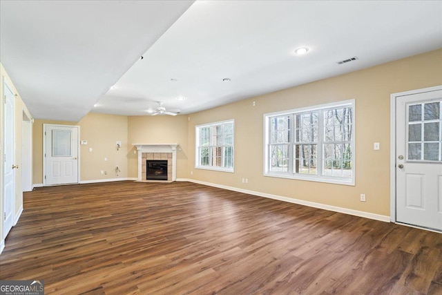 unfurnished living room featuring a ceiling fan, wood finished floors, visible vents, baseboards, and a tiled fireplace