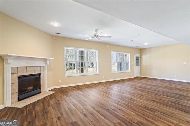 unfurnished living room with visible vents, a ceiling fan, a tiled fireplace, wood finished floors, and baseboards