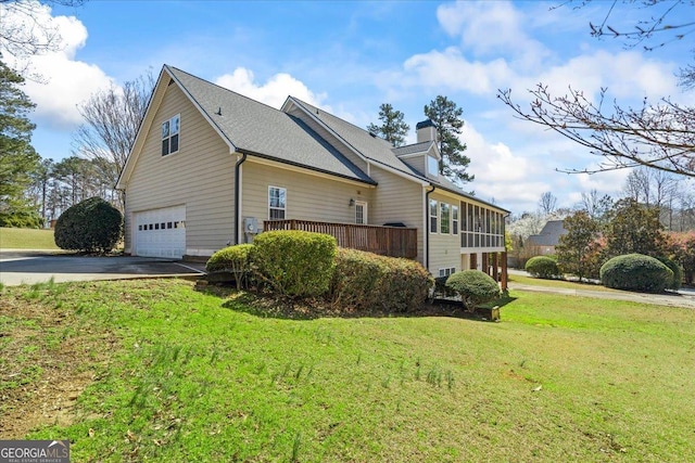 view of home's exterior with an attached garage, a yard, a sunroom, a chimney, and aphalt driveway