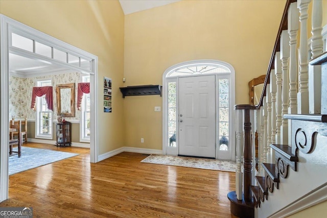 foyer entrance with wallpapered walls, baseboards, stairs, a high ceiling, and wood finished floors