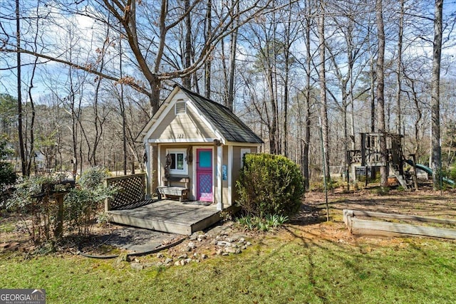 view of outdoor structure with an outbuilding, a playground, and a view of trees