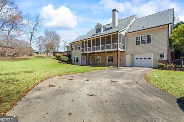 rear view of property featuring cooling unit, a chimney, a yard, a sunroom, and driveway