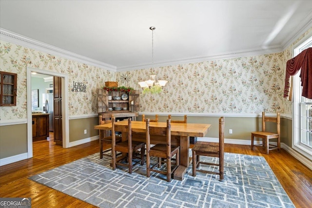 dining space with a notable chandelier, a wainscoted wall, wallpapered walls, and wood finished floors