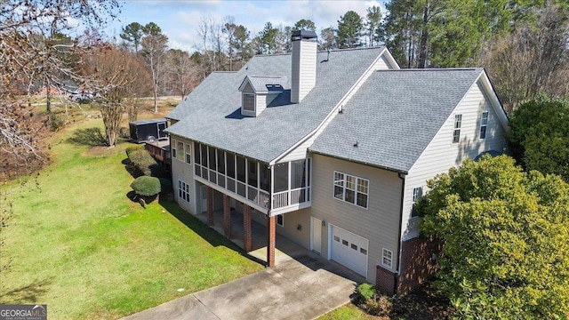 back of house featuring a lawn, driveway, a sunroom, a garage, and a chimney