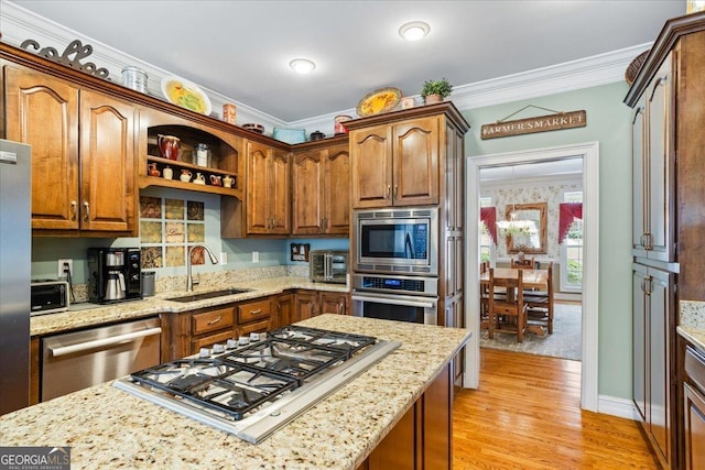 kitchen featuring ornamental molding, light stone counters, light wood-style floors, stainless steel appliances, and a sink