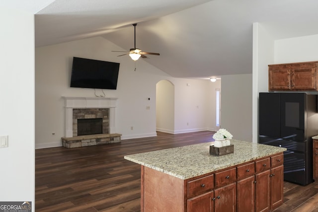 kitchen featuring open floor plan, a stone fireplace, arched walkways, a ceiling fan, and dark wood-style flooring