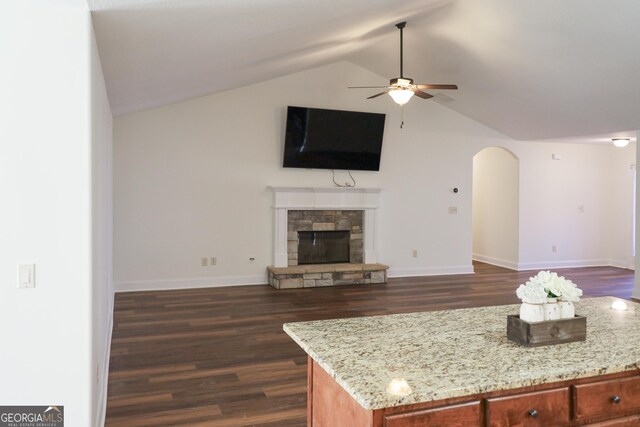 kitchen with open floor plan, arched walkways, a fireplace, light stone countertops, and vaulted ceiling