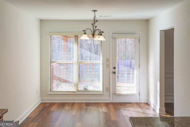 unfurnished dining area with a notable chandelier, wood finished floors, and baseboards