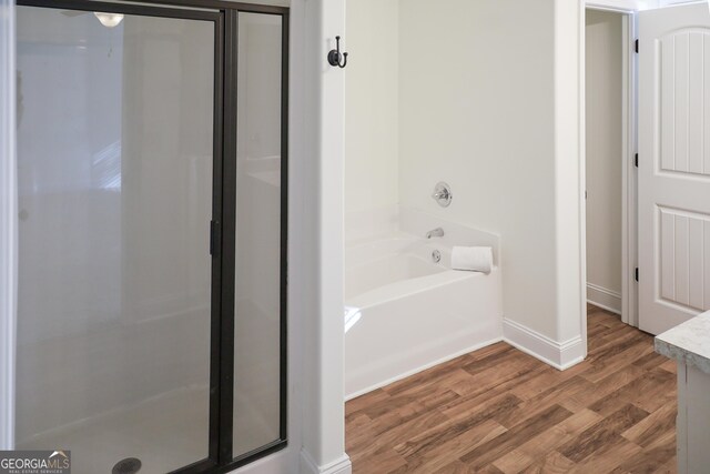 bathroom with baseboards, wood finished floors, a shower stall, and a bath