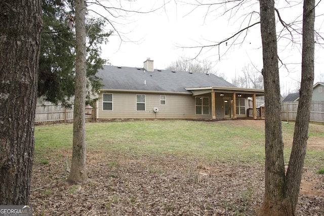 rear view of property with a yard, fence, and a chimney