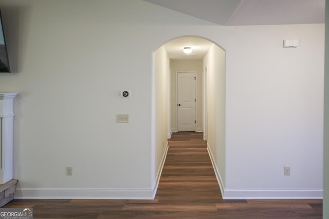 hallway with vaulted ceiling, baseboards, arched walkways, and dark wood-style flooring