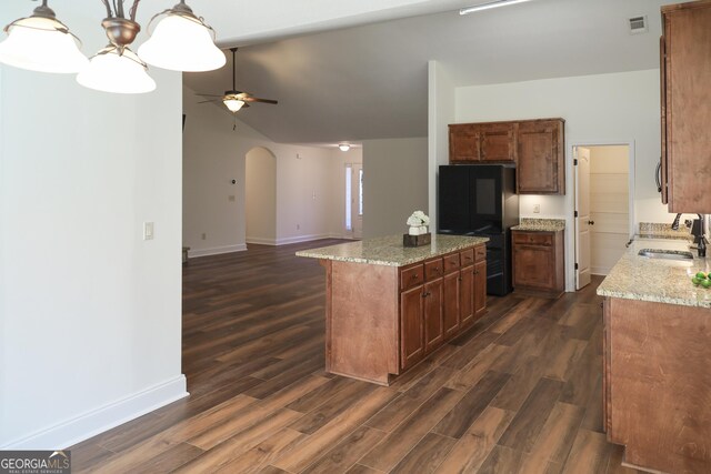 kitchen featuring a sink, dark wood finished floors, a center island, freestanding refrigerator, and arched walkways