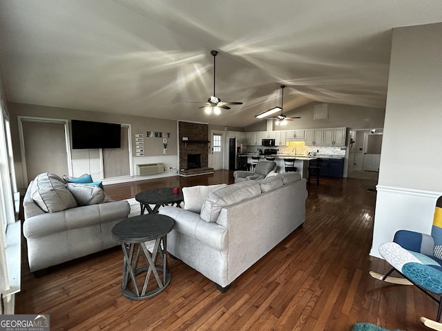 living area featuring a fireplace, vaulted ceiling, dark wood-style floors, and a ceiling fan