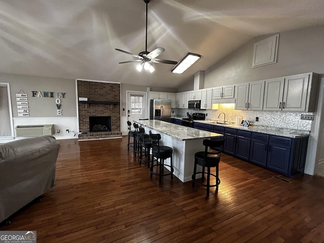 kitchen featuring ceiling fan, dark wood finished floors, open floor plan, a kitchen bar, and stainless steel appliances