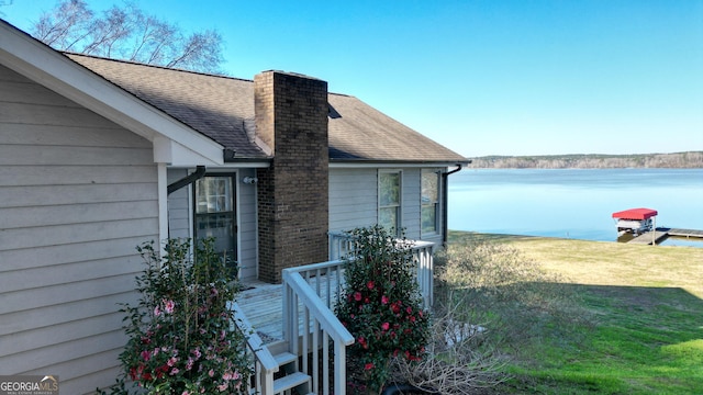 exterior space with a yard, a chimney, roof with shingles, and a water view