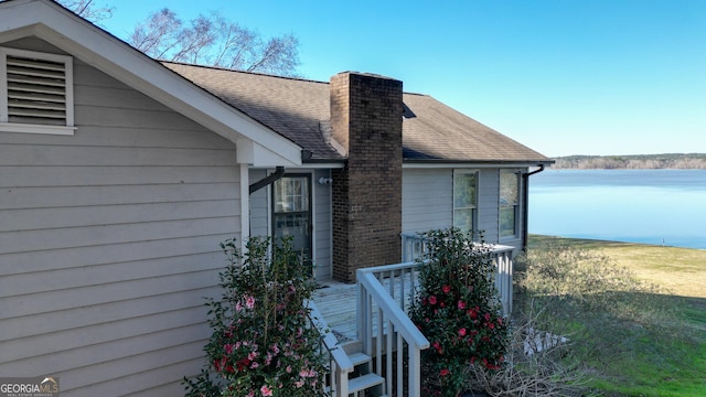 exterior space with a chimney, roof with shingles, and a water view