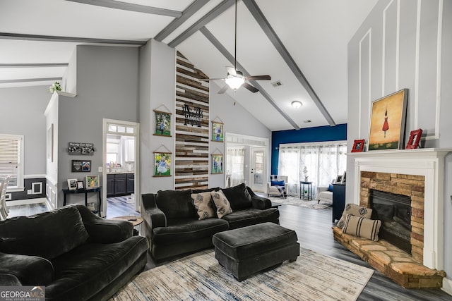 living area with visible vents, beamed ceiling, high vaulted ceiling, wood finished floors, and a stone fireplace