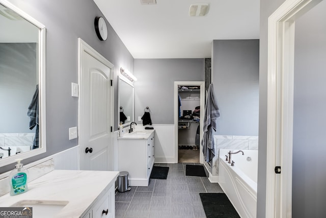 full bath featuring a walk in closet, two vanities, a sink, wainscoting, and a bath