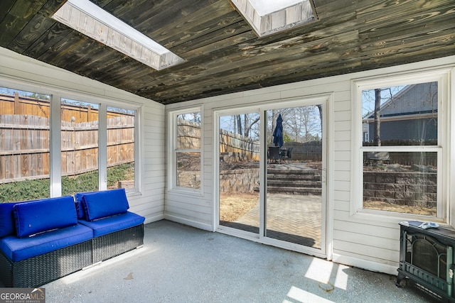 sunroom featuring wooden ceiling, a wood stove, a wealth of natural light, and lofted ceiling with skylight