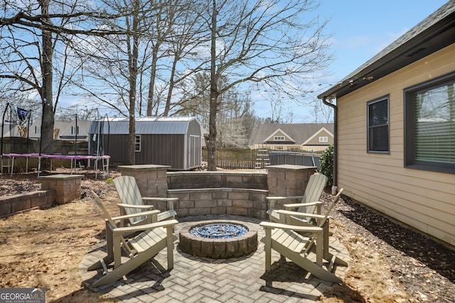 view of patio / terrace with a trampoline, a fenced backyard, a shed, a fire pit, and an outdoor structure