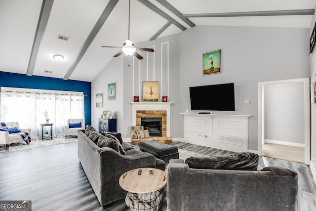 living area featuring wood finished floors, visible vents, high vaulted ceiling, a fireplace with raised hearth, and beamed ceiling