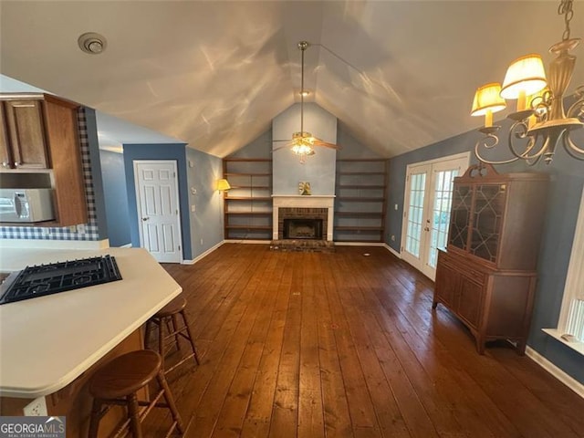 interior space featuring ceiling fan with notable chandelier, dark wood-type flooring, a fireplace, and vaulted ceiling