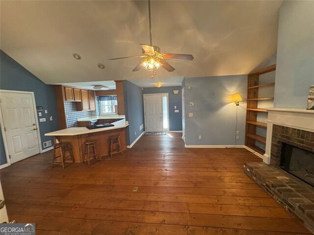 kitchen with lofted ceiling, a peninsula, a fireplace with raised hearth, and dark wood finished floors