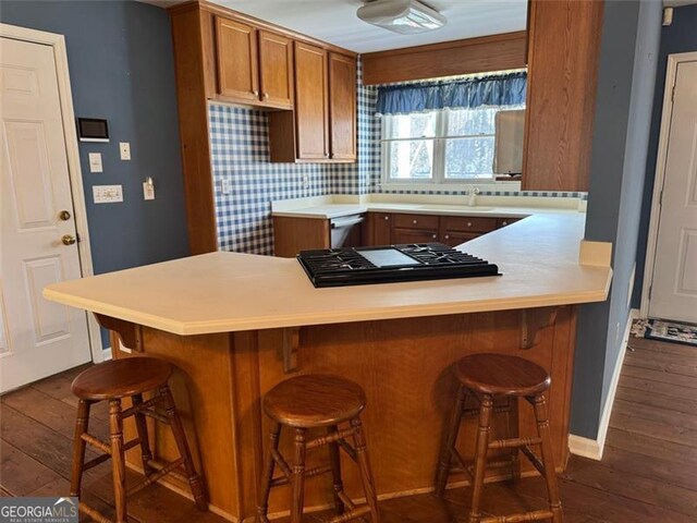 kitchen with dark wood-type flooring, light countertops, brown cabinets, a peninsula, and a sink