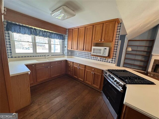 kitchen featuring a sink, backsplash, dark wood-style floors, white microwave, and stainless steel range with gas stovetop