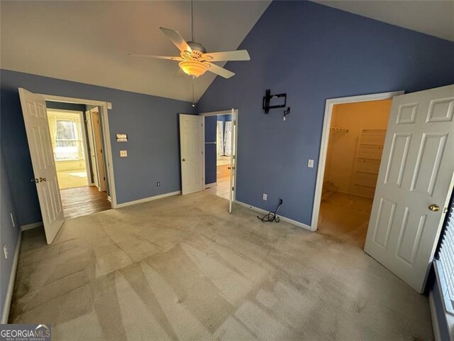 unfurnished bedroom featuring a walk in closet, high vaulted ceiling, baseboards, and light carpet