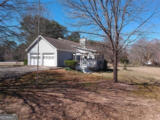 view of side of home with an attached garage, a chimney, driveway, and a deck